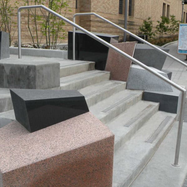 Side View of Concrete Stairs and Rail Lined with Blocks of Geometric Granite in Many Shapes, Colors, and Finishes.