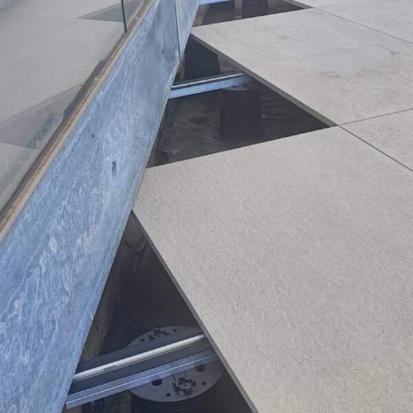 Edge detail with exposed membrane, PB pedestals, E-BRS rails, and porcelain pavers.
