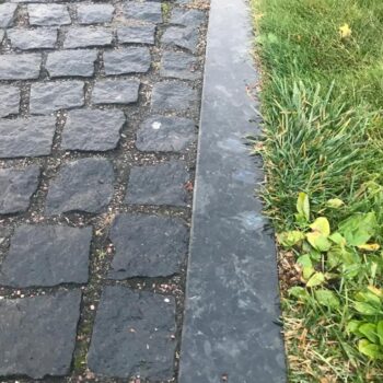 Black Sea Blue Granite cobble-size pavers spaced evenly next to a matching curbstone.