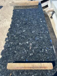 Large Black Sea Blue Granite slab resting on wood blocks, showing blue iridescence in the stone surface.