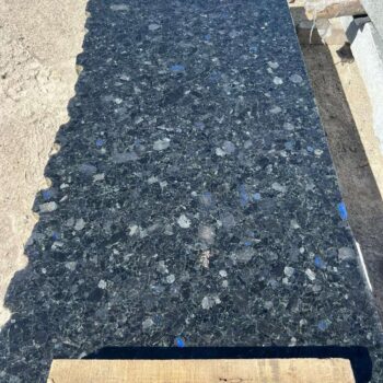 Large Black Sea Blue Granite slab resting on wood blocks, showing blue iridescence in the stone surface.