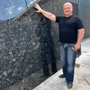 Standing Beside a Very Large Black Sea Blue Granite Slab, Showcasing its Scale and Surface Finish.
