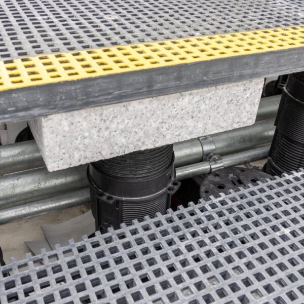 Close-up of grating panel edge with ballast and conduit visible beneath pedestal system