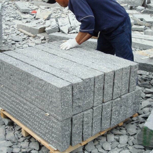 Worker inspecting Bigio Grey granite kerbstones with pineapple stone finish, emphasizing craftsmanship and quality control.