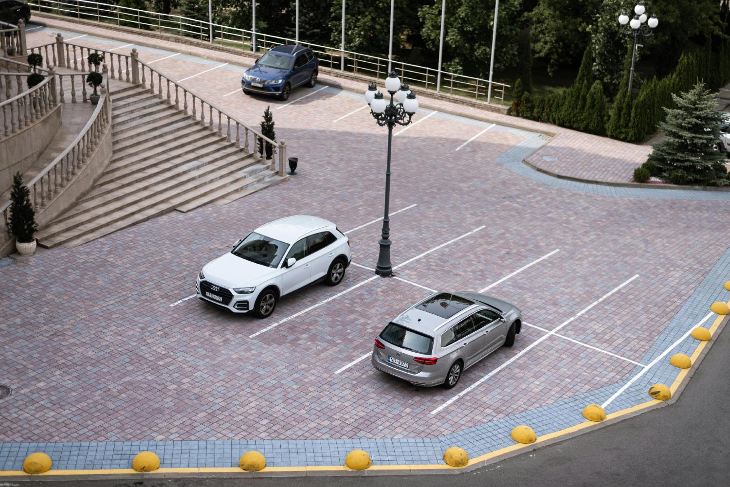 Three cars parked in an elegant outdoor space with parking lot pavers and surrounding trees.
