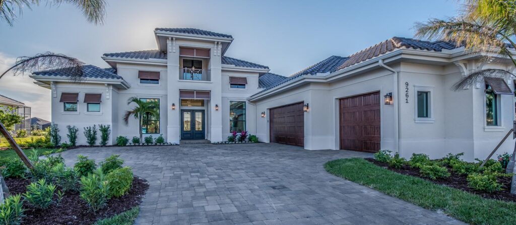 Large natural stone permeable driveway pavers leading to a two-car garage with palm trees and landscaped lawn edges.
