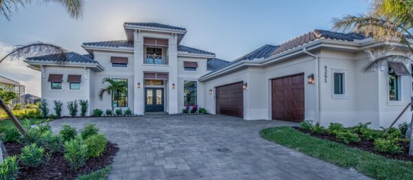 Large natural stone permeable driveway pavers leading to a two-car garage with palm trees and landscaped lawn edges.