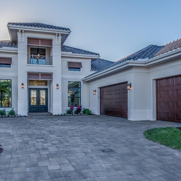 Large natural stone permeable driveway pavers leading to a two-car garage with palm trees and landscaped lawn edges.