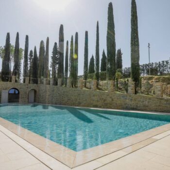 Rosca Gold porcelain paver pool deck surrounding a luxury swimming pool with arched stone walls in the background.