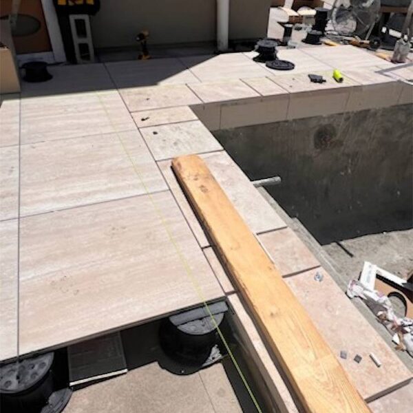 Exposed Buzon pedestals at the edge of a porcelain paver pool deck during construction.