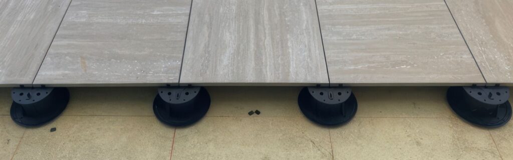 Porcelain paver installation over Buzon adjustable pedestals with substrate showing.