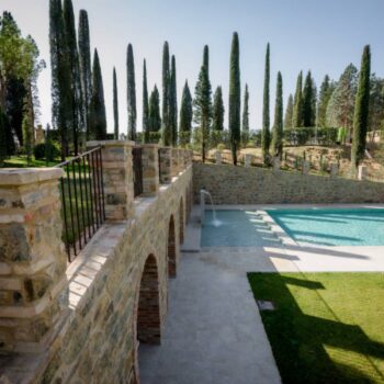 Luxury swimming pool with Rosca Gold porcelain paver surround and crenellated stone walls featuring arched openings.