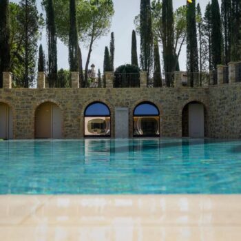 Rosca Gold porcelain paver pool deck surrounding a luxury swimming pool with arched stone walls in the background.
