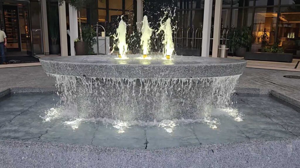 Stone-paved commercial entrance leading to a fountain and a hotel building facade.
