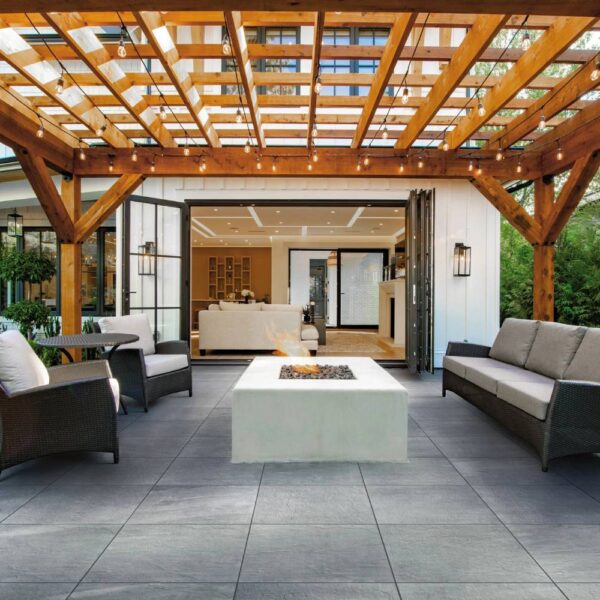 Blustone 24x24-inch porcelain pavers create an outdoor room with lounge seating, fire pit, a pergola, and a folding glass wall.