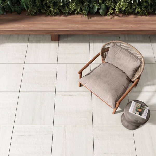 Marmo White 24x24-inch porcelain pavers surround a comfortable outdoor seating area with a wood and wicker chair, side table, and wooden bench.