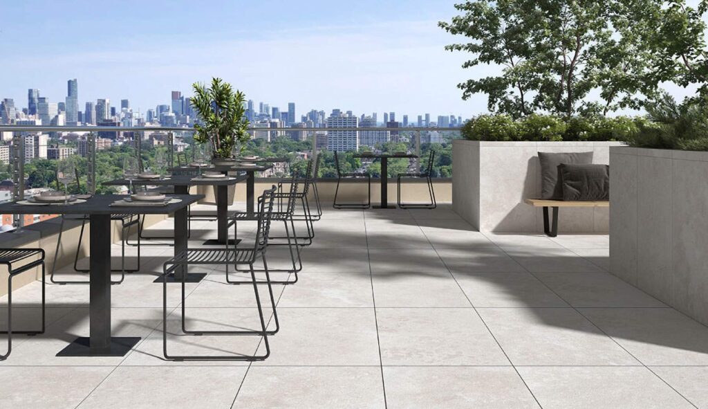 Trevino Ivory travertine-look porcelain pavers on an elevated rooftop terrace overlooking a city.